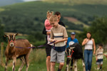 An image of a boy smiling whilst walking a goat in the foreground, with his family following behind.