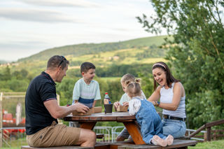 An image of a family enjoying their food from a picnic bench, surrounded by gorgeous views and outdoor play.