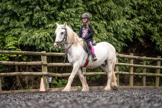 An image of a girl riding a small white horse around Cantref Riding Centre's training area.