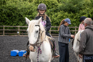 An image of a girl smiling on horseback whilst her sister gets her stirrups altered.